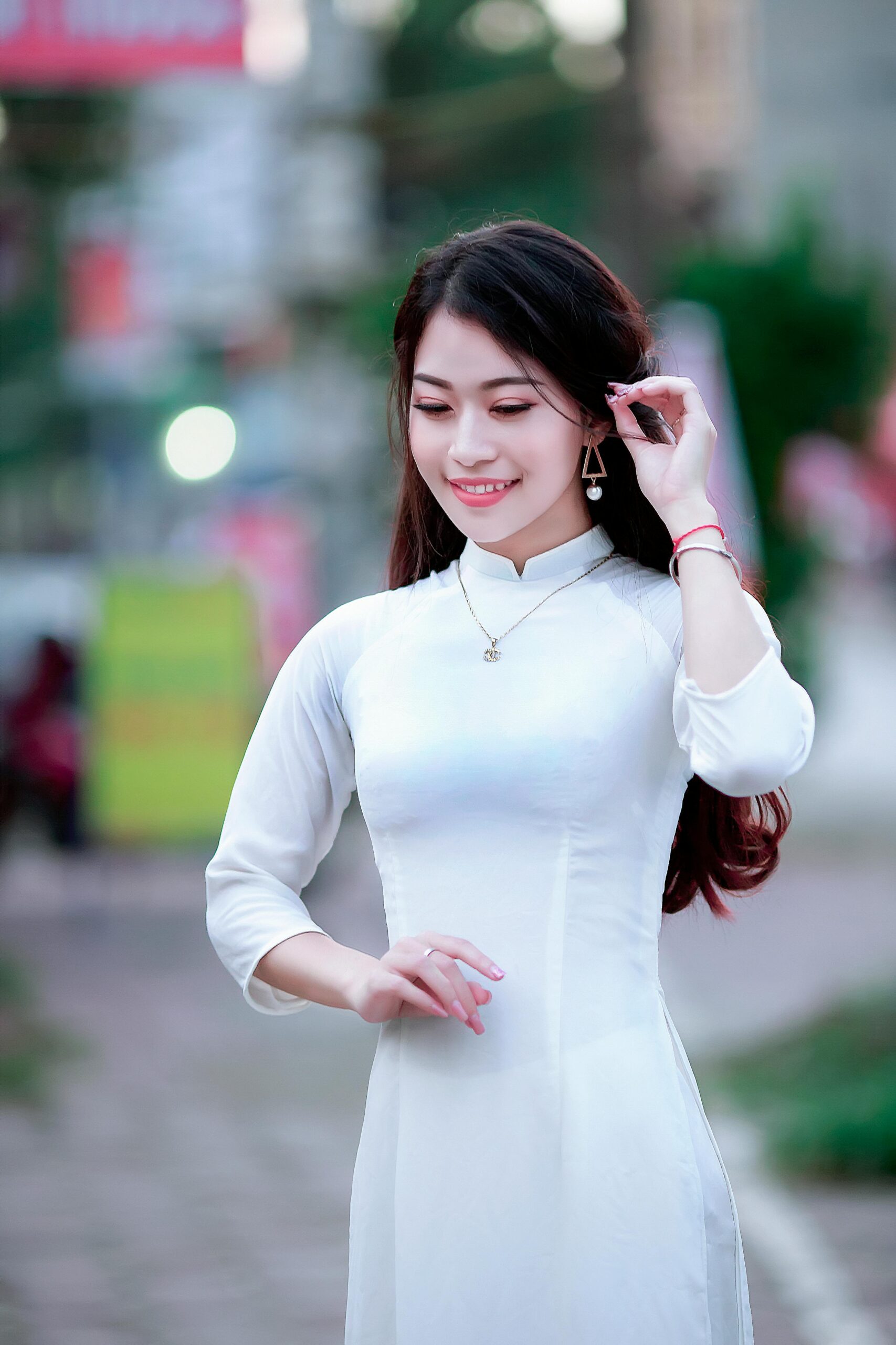 A woman in a white Ao Dai poses gracefully outdoors, showcasing traditional Vietnamese fashion.
